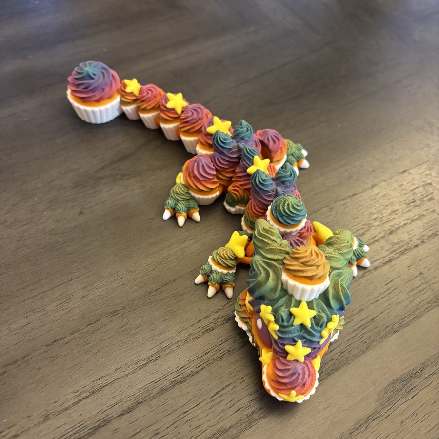 Articulated cupcake dragon 3D printed in rainbow colors with frosting-swirl scales and yellow stars
