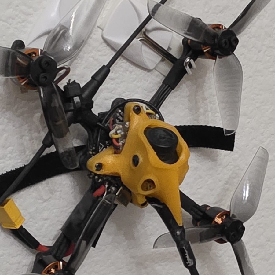 FPV micro drone with a custom 3D printed yellow TPU canopy, wall-mounted