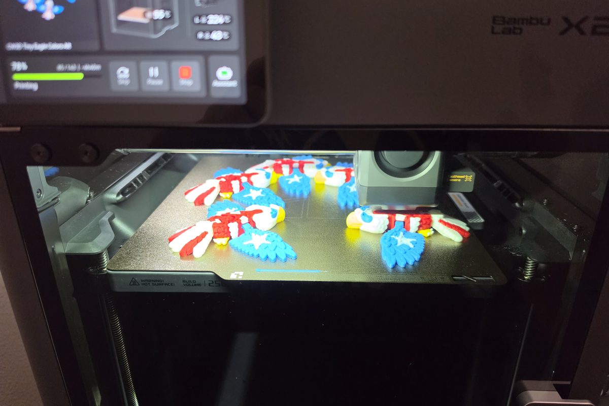 Bambu Lab X2D printer mid-print with a build plate full of red, white and blue eagles